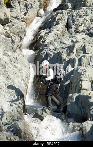 Nuova Zelanda, Isola del Sud, Arthurs Pass National Park. Anne Leicher stepping attraverso il Fiume Bianco vicino la testa acque. Foto Stock