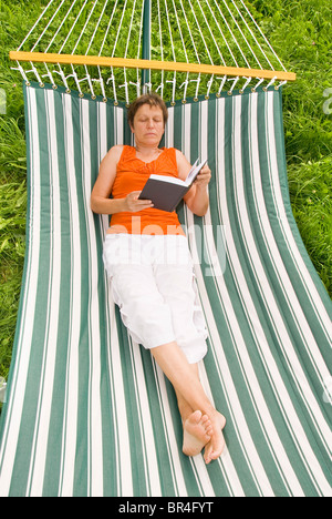 Senior donna a leggere un libro mentre giaceva in una amaca Foto Stock