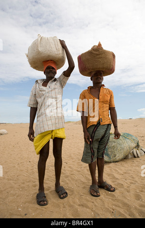 Due pescatori portano sul loro capo un paniere di beni sulla spiaggia vicino al villaggio di pescatori di Gopalpur on Sea, Orissa, India. Foto Stock