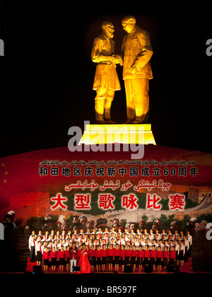 La prestazione della coltura sotto una statua di Mao e un senior Uyghur uomo ad Hotan Xinjiang in Cina. Foto Stock