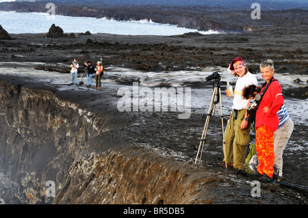 Gruppo di turisti sul bordo del cratere la visione di lava fusa che scorre verso il mare del vulcano Kilauea, isole Hawaii, Stati Uniti Foto Stock