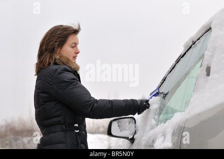 Giovane donna di pulizia vetri auto da neve nella stagione invernale Foto Stock