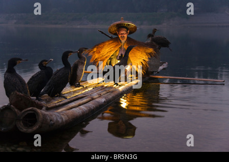 Fisherman indossando la paglia umettare la pesca con i cormorani su zattera di bambù sul Fiume Li al crepuscolo, Yangshuo, Guangxi, Cina Foto Stock