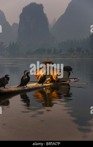 Fisherman indossando la paglia umettare la pesca con i cormorani su zattera di bambù sul Fiume Li al crepuscolo, Yangshuo, Guangxi, Cina Foto Stock