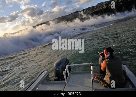 Donna sul battello a vapore fotografare rising off la lava scorre in oceano, vulcano Kilauea, isole Hawaii, Stati Uniti d'America. Foto Stock