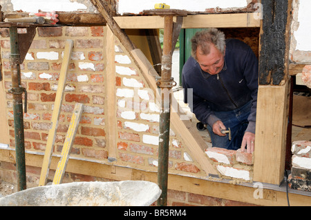 Il rinnovamento di un vecchio legno incorniciata edificio muratore formando una nuova parete con mattoni vecchi e nuovi di travi di quercia su una parete esterna Foto Stock