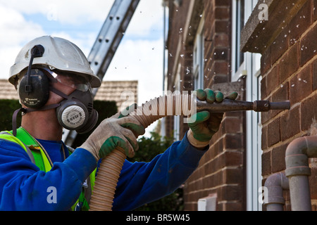 Parete di cavità di isolamento viene installata in una casa a Kirklees, UK. I fori sono praticati nella parete e schiuma pompata a. Foto Stock