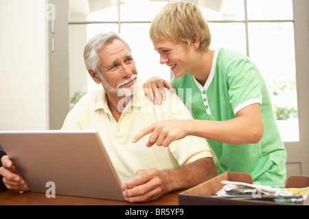 Nipote di adolescenti aiutando nonno per uso portatile a casa Foto Stock