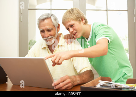 Nipote di adolescenti aiutando nonno per uso portatile a casa Foto Stock