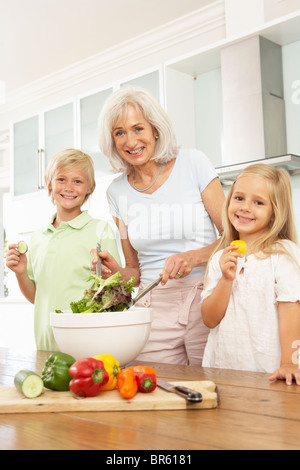 Nipoti aiutando la nonna a preparare insalata in cucina moderna Foto Stock