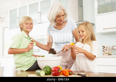 Nipoti aiutando la nonna a preparare insalata in cucina moderna Foto Stock