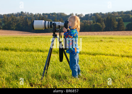 Ragazzo che guarda attraverso super teleobiettivo sulla fotocamera digitale Foto Stock