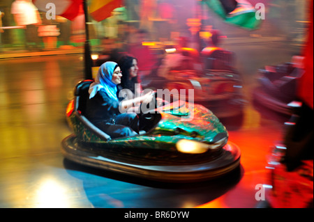 Una donna musulmana in un hijab gode di se stessa sul dodgems ad una fiera Foto Stock