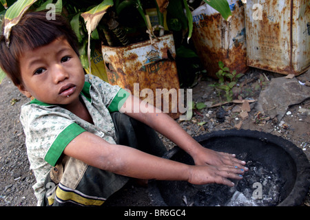 Un ragazzo giovane che vive in un squatter la baracca con la sua famiglia di sei tenta di riscaldarsi in un freddo giorno di Kampong Cham, Cambogia. Foto Stock