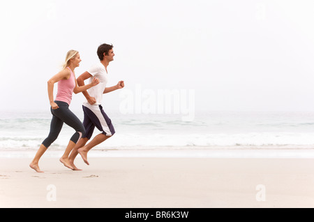 Coppia giovane che corre lungo la spiaggia di inverno Foto Stock