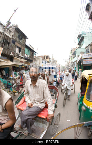Indian uomo corse in rickshaw su strada affollata a Delhi in India. Foto Stock