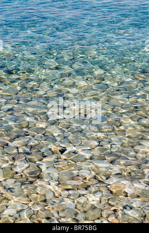 Il sole che splende attraverso il mare su ciottoli su una spiaggia a Paxos, Grecia Foto Stock