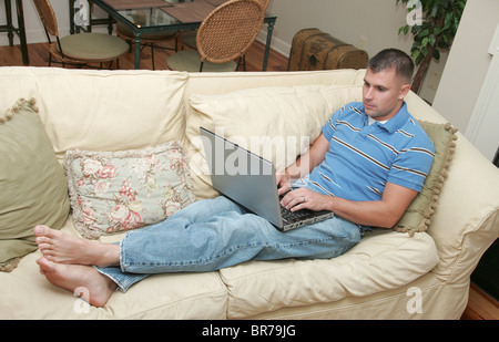 Un giovane uomo che lavora su un computer portatile da un caminetto a casa Foto Stock