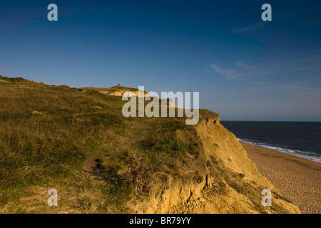 Figura distante con il loro cane, godendo di sera la luce solare su una scogliera che si affaccia sulla spiaggia come la marea avanza a Burton Br Foto Stock