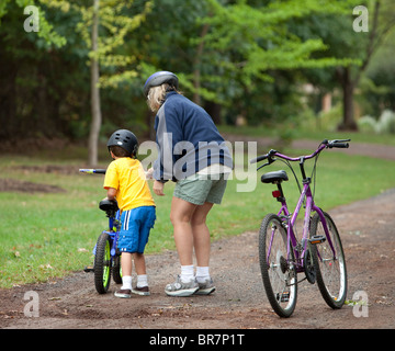 Una madre aiuta il suo giovane figlio con la sua bicicletta. Insegnare al bambino come un giro in bicicletta. Foto Stock