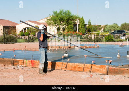 Un lavoratore edile termina una nuova colata di calcestruzzo soletta con un attrezzo di flottazione. Foto Stock