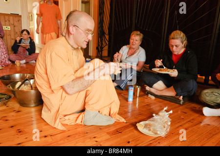 Hare Krishna devoto indossando abiti dello zafferano spiega la sua religione per ospiti in un Hare Krishna temple room Foto Stock