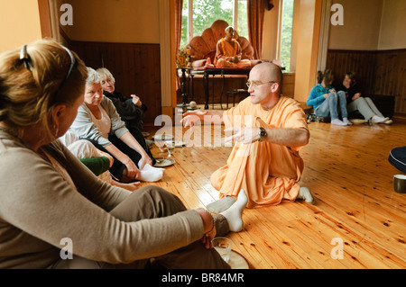 Hare Krishna devoto indossando abiti dello zafferano spiega la sua religione per ospiti in un Hare Krishna temple room Foto Stock