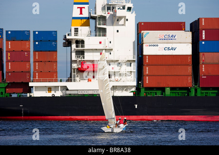 Una barca a vela di dare il via ad una nave portacontainer nel trafficato porto di Charleston, South Carolina, Stati Uniti d'America. Foto Stock