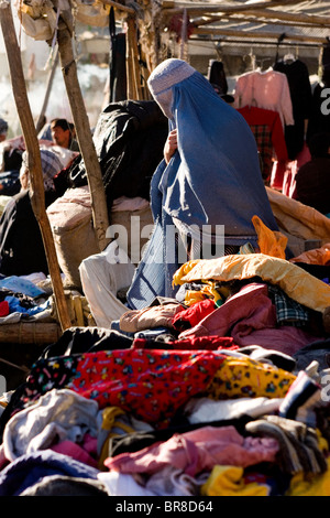 Una donna in burqa fa il suo modo attraverso i fornitori delle tabelle di abiti e prodotti tessili in un mercato di Kabul, Afghanistan. Foto Stock