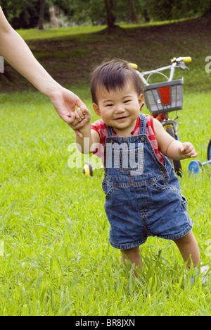 Baby boy walking supportato dalla madre la mano Foto Stock