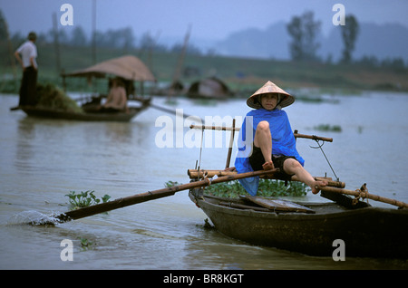 Donna remare una barca con i suoi piedi vicino Tam Coc Vietnam. Foto Stock