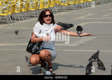 Un turista alimentazione dei piccioni in Piazza San Marco a Venezia Foto Stock