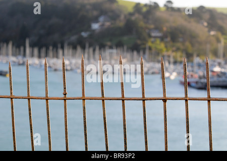 Vecchia ruggine sottile cast-ringhiere in ferro su una strada di Dartmouth con barca a montanti in Kingswear sul fiume Dart in background Foto Stock