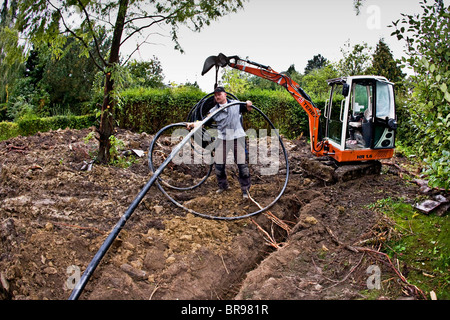 I tubi per il riscaldamento geotermico sistema essendo scavato da un escavatore meccanico Foto Stock