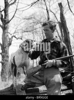 1930s uomo HUNTER INDOSSANDO PLAID FLANNEL SHIRT E I JODHPURS seduta sul LOG AZIENDA PETTING SHOTGUN cane puntatore Foto Stock