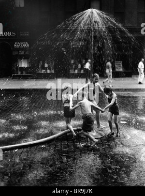 1930s interna della città dei bambini che giocano in spray da idrante antincendio sprinkler acqua Foto Stock