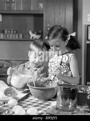 Anni sessanta due bambini ragazza ragazzo ciotola versare la miscelazione di latte IN CUCINA Foto Stock