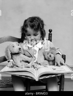1930s LETTURA DELLA RAGAZZA STORYBOOK al suo cane giocattolo e orsacchiotto Foto Stock