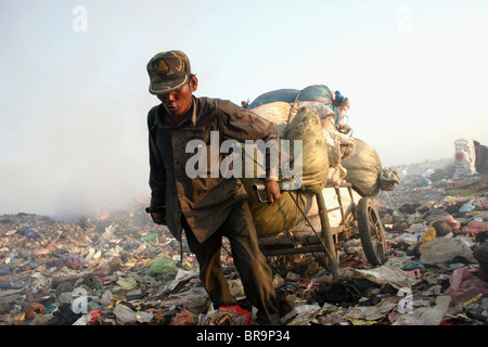 Un lavoratore di sesso maschile cale di materiale riciclabile con un carrello di acciaio presso il pungo Meanchey discarica in Phnom Penh Cambogia. Foto Stock