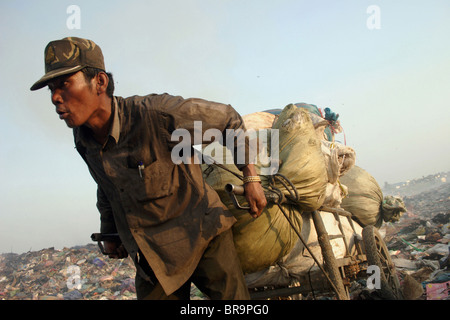 Un lavoratore cale di materiale riciclabile con un carrello di acciaio presso il pungo Meanchey discarica in Phnom Penh Cambogia. Foto Stock