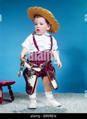 Anni sessanta baby boy bambino in piedi indossando il cappello da cowboy RED PLAID SHORTS fondina con pistole pistole Foto Stock