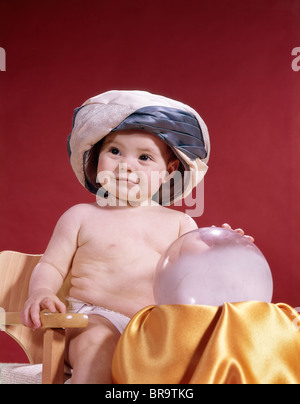 Anni sessanta BABY FORTUNE TELLER indossando turbante seduto con sfera di cristallo Foto Stock