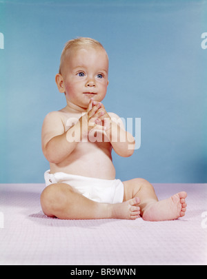 Anni sessanta BABY indossa pannolini panno seduto con le mani insieme riflessivo pongono l'espressione Foto Stock