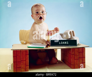 Anni sessanta imprenditore bambino seduto alla scrivania giocattolo prestiti segno indossando occhiali da vista guardando la fotocamera Foto Stock
