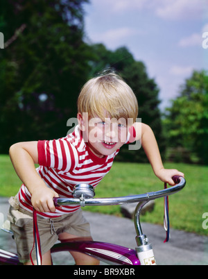 Anni Settanta anni sessanta sorridente ragazzo biondo SPORGENDOTI manubri di bicicletta guardando la fotocamera Foto Stock