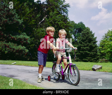 Anni sessanta anni settanta BOY aiutare piccolo fratello RIDE DUE RUOTE BICICLETTA CON RUOTE DI FORMAZIONE Foto Stock