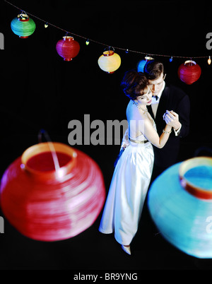 Anni Settanta matura in abiti formali danzando sotto carta colorata lanterne cinesi Foto Stock