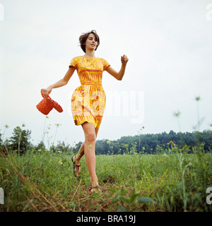 Anni Settanta giovane donna indossa colorato abito di stampa in esecuzione in campo rosso che portano cappello di paglia Foto Stock