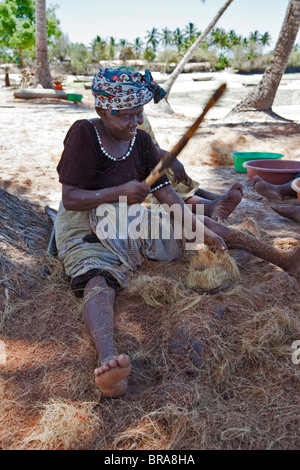 , Kizimkazi Dimbani, Zanzibar, Tanzania. Donna battendo gusci di noce di cocco per produrre filati di cocco, per realizzare corde. Foto Stock