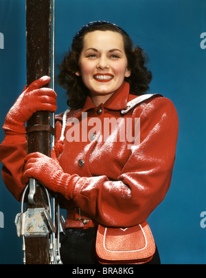 Negli anni quaranta anni cinquanta sorridente BRUNETTE DONNA CON GLI SCI giacca rossa leggermente spolverata di neve Foto Stock